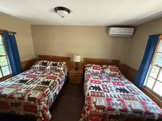 Two beds with animal-themed quilts, nightstand, lamp, and windows with blue curtains in a bedroom.