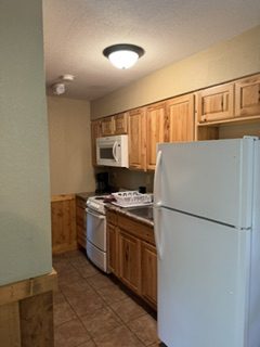 Small kitchen with wooden cabinets, white fridge, and tiled floor.