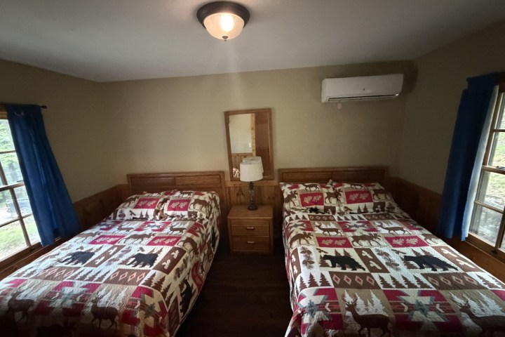 Two beds with patterned quilts in a cozy room, separated by a wooden nightstand.
