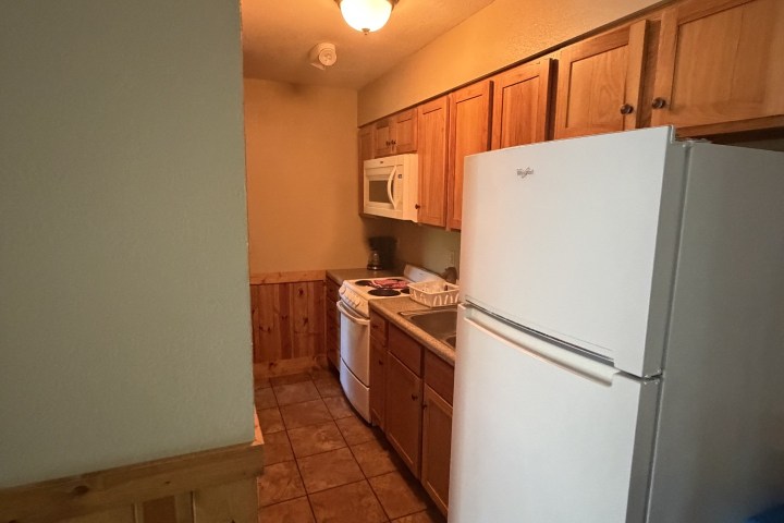 Narrow kitchen with tile floor, wooden cabinets, stove, microwave, and refrigerator.
