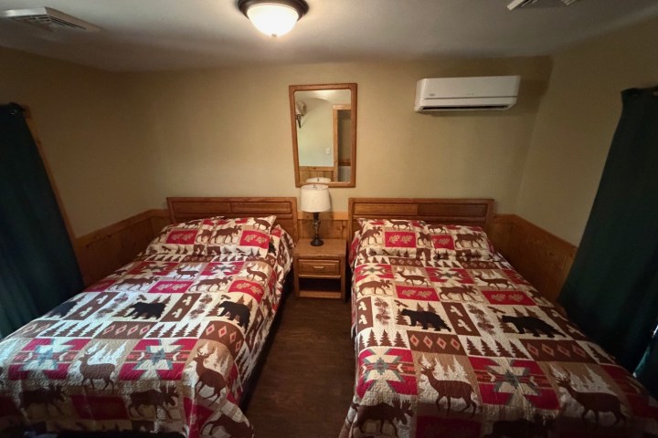 Two beds with patterned quilts and a lamp in a cozy room.