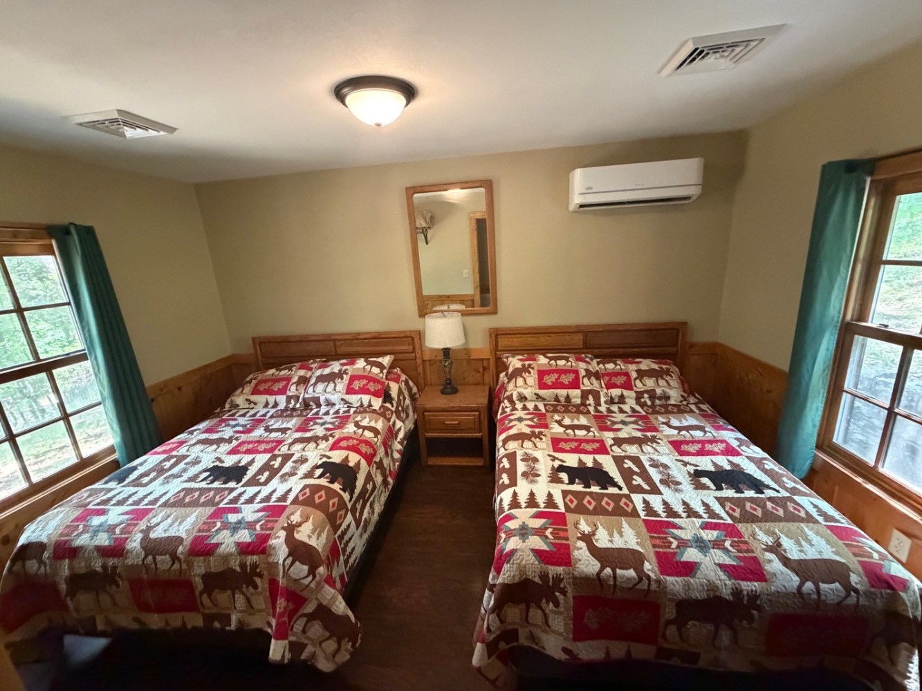 Two beds with patterned quilts, lamp, and window in cozy room.
