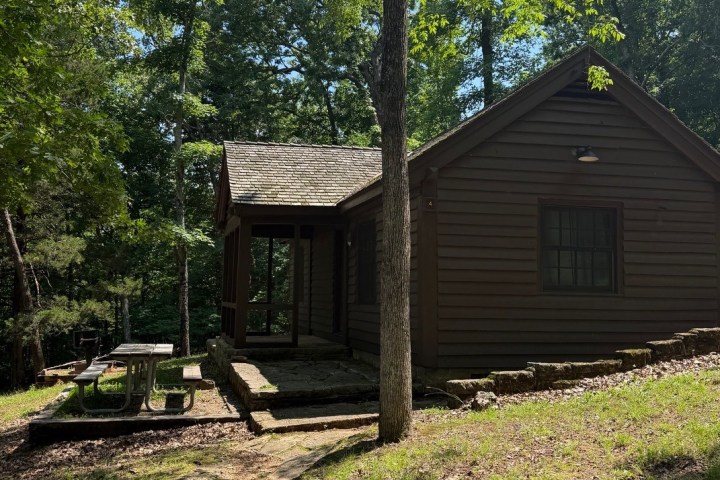 Small wooden cabin surrounded by trees with a picnic table outside.
