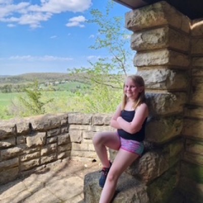 Girl smiling, sitting on stone wall with scenic landscape view.