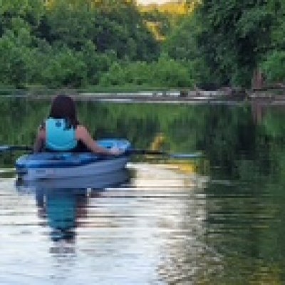Person kayaking on a calm river surrounded by lush green trees.