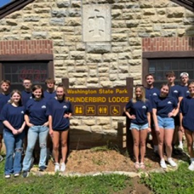 Group of people in matching navy shirts standing by Thunderbird Lodge sign, stone building in the background.